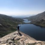 Person standing at a mountain edge looking out to the lake in front of them