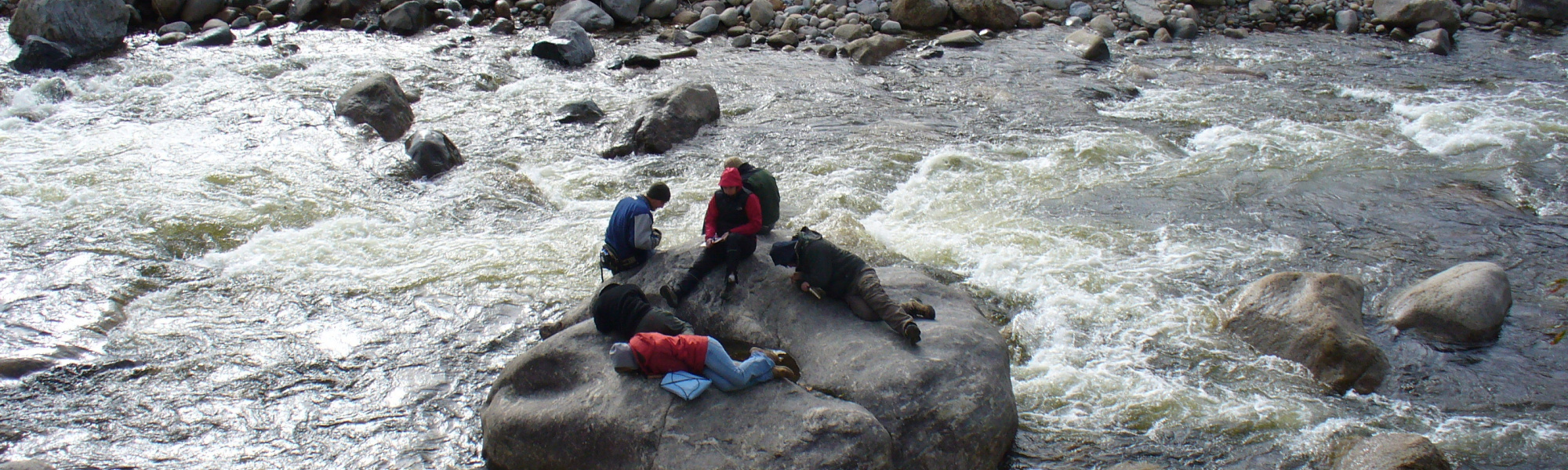 5 people sitting on a rock in the middle of a river conducting fieldwork