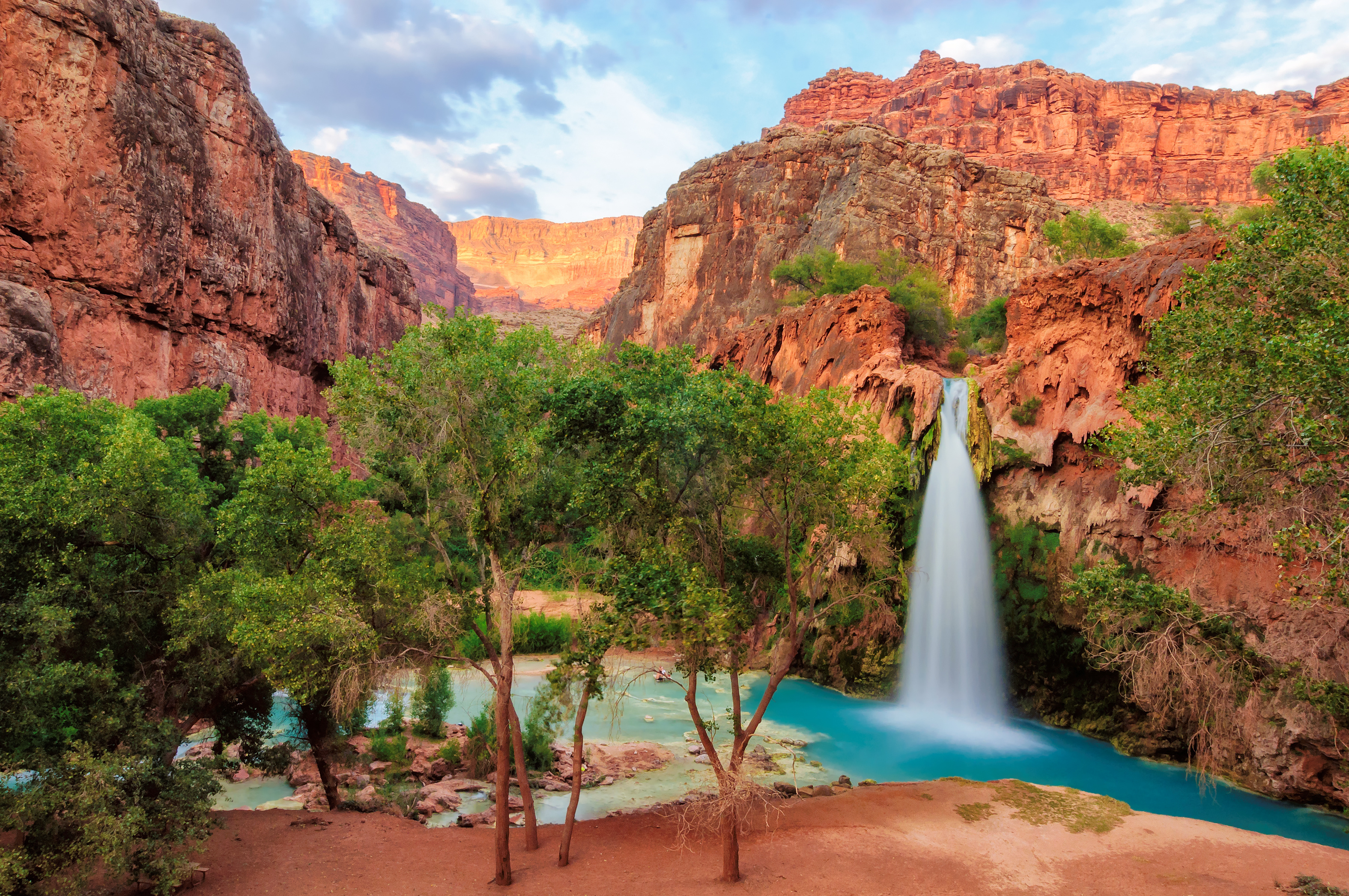 Cove in the desert with small waterfall, red rock and green trees