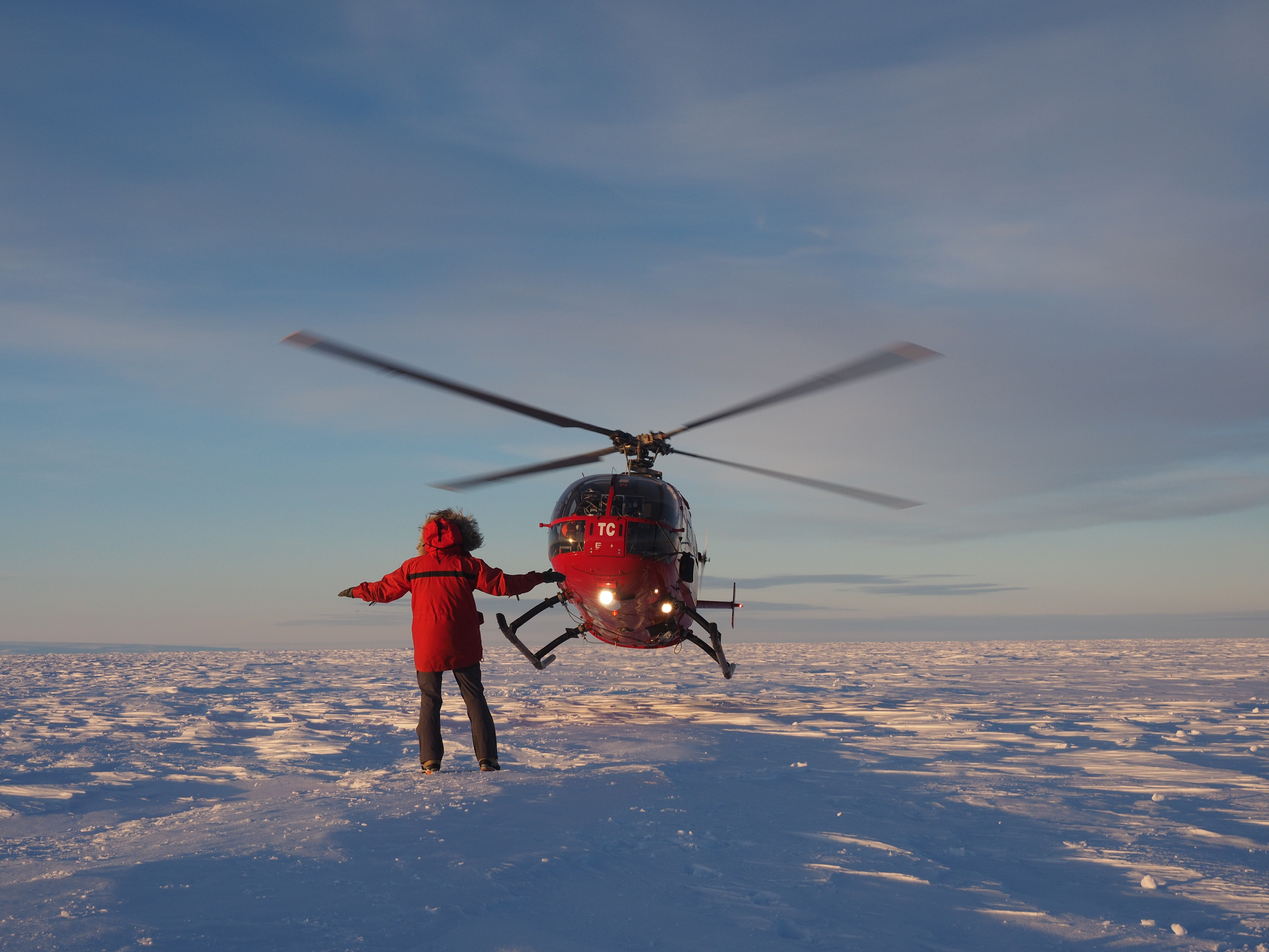 Helicopter landing with someone directing it over a snowy terrain