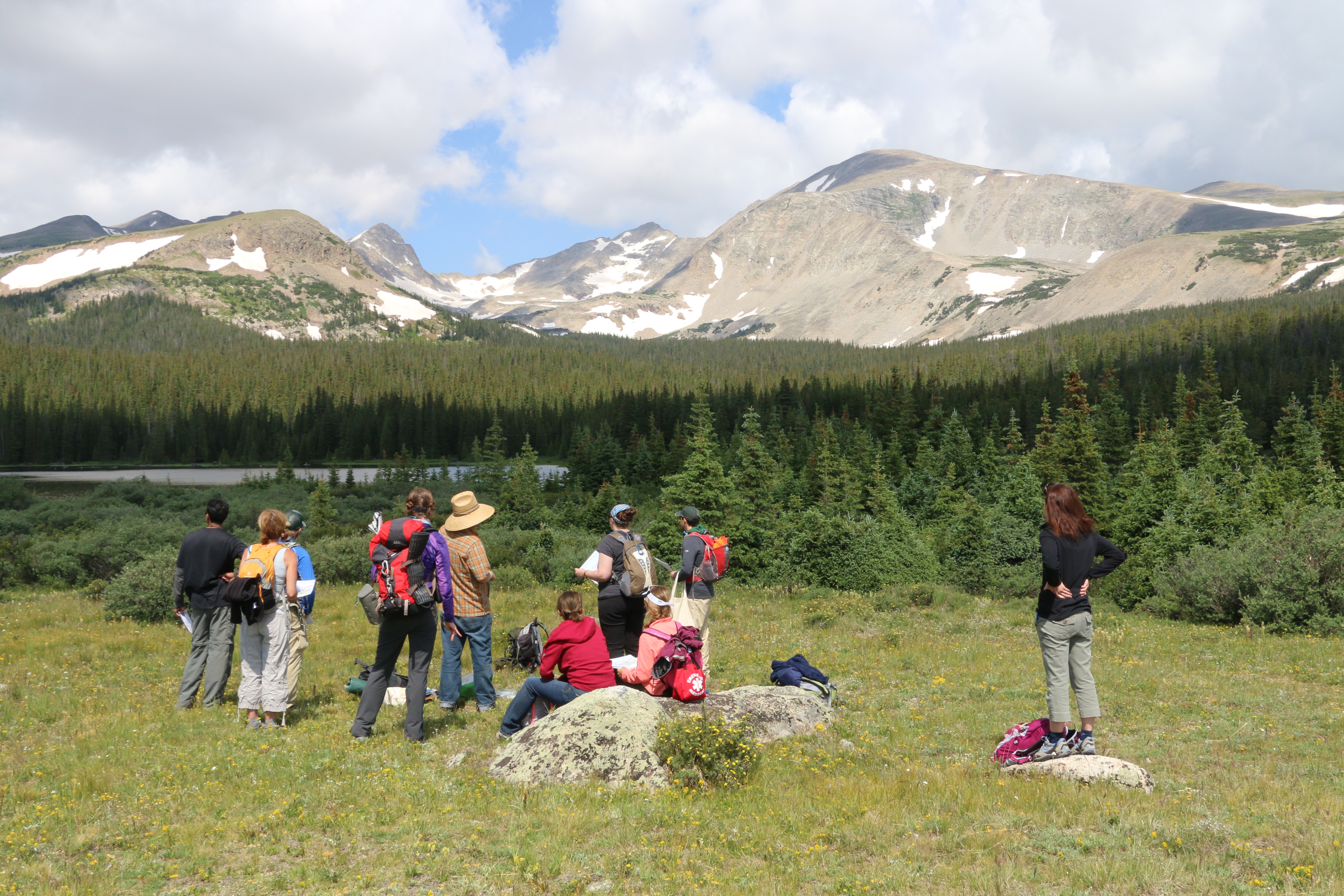 Students apart of the RECCS program standing in the middle of a field in the mountains with backpacks on