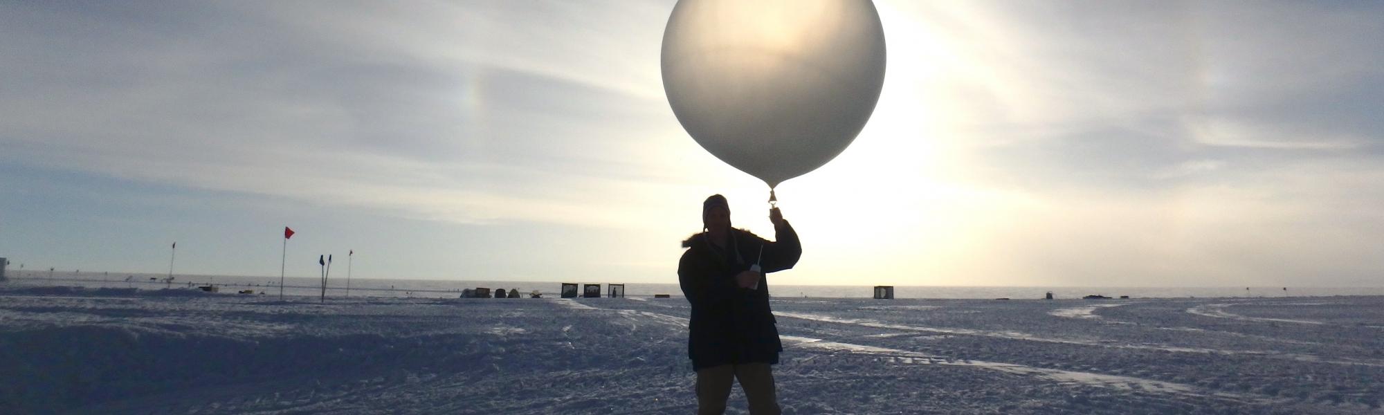 Person holding a clear balloon on an ice field with the sun in the back