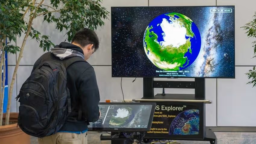 Person looking down at an interactive SOS exhibit board with the a globe on the tv in front of the person