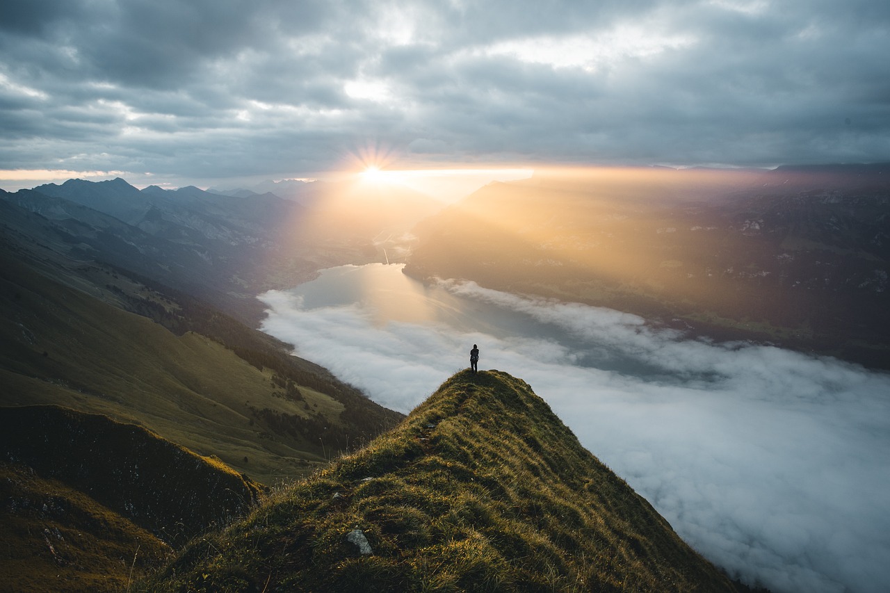 Person standing on top of mountain, sun rising in the back with ocean in the horizon