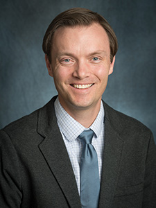Russ Schumacher smiles at the camera with a dark blue background