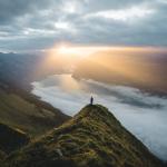 Person standing at a cliff looking out to the river and mountains landscape