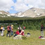 People standing in field below mountains looking out in the distance