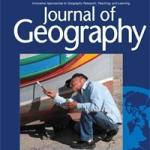 Dark‑blue journal cover titled Journal of Geography in bold white type at the top. Below the title is a photograph of a tall indoor waterfall surrounded by lush greenery under a glass‑panel dome. On the right edge of the cover, a semi-transparent world map motif in blue fades toward the bottom.