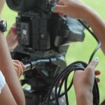 Close-up of people setting up a professional video camera, with one person adjusting controls and another holding cables