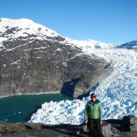 Dr. Twila Moon stands in front of melting snowpack and a distance mountain.