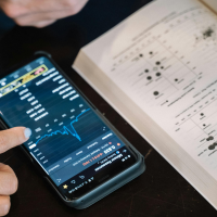 A hand scrolls on a phone aside a textbook.