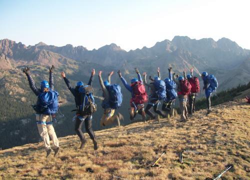 Group of people outside in rock climbing gear facing away from the camera and jumping