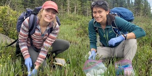 Two people smiling at the camera, crouching down in grass