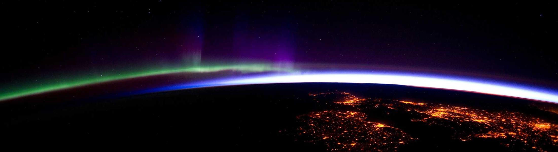 NOAA image of Earth's horizon from space you can see a green light on one side and a blue light on the other side of the horizon and some cities lit up from space on the Earth