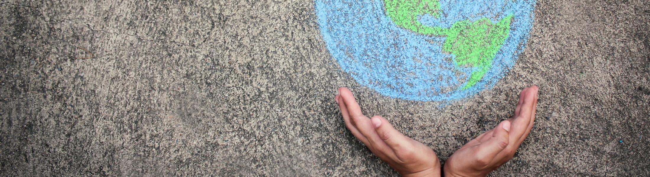 childs hands holding a chalk drawing of the world