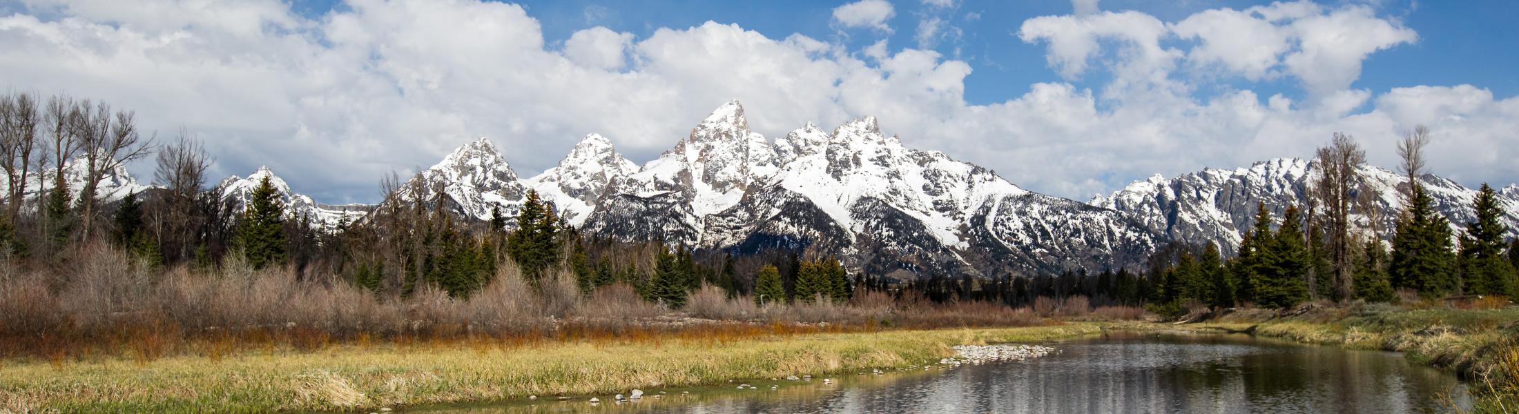 Picture of a snowy mountain range with blue sky and river running through it