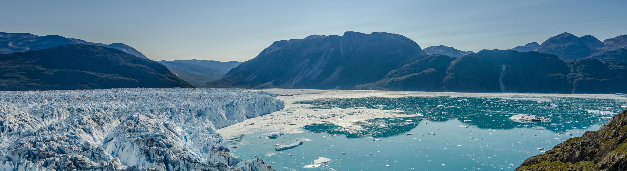 Glacier with blue water and mountain range in the background, no clouds in the sky