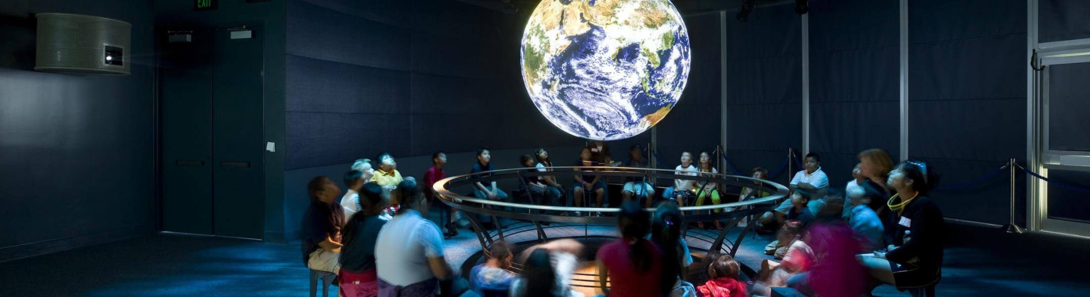 Students sit around a NOAA Science on a Sphere.