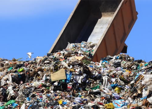 A large truck dumps trash into a landfill.