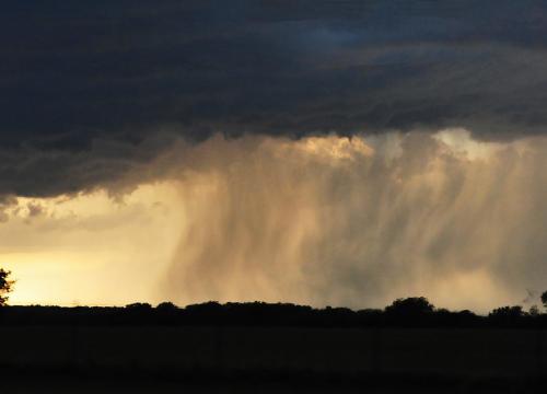Dark cloud at top of image raining down onto shadowed lands with yellow sunlit sky in the middle