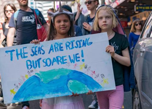 Two girls standing side by side holding a sign that reads "The seas are rising but so are we!"