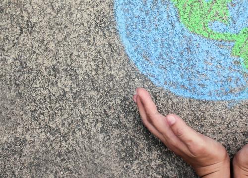 childs hands holding a chalk drawing of the world