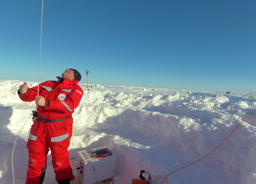 Person in red suit in the Arctic pulling down a large orange balloon