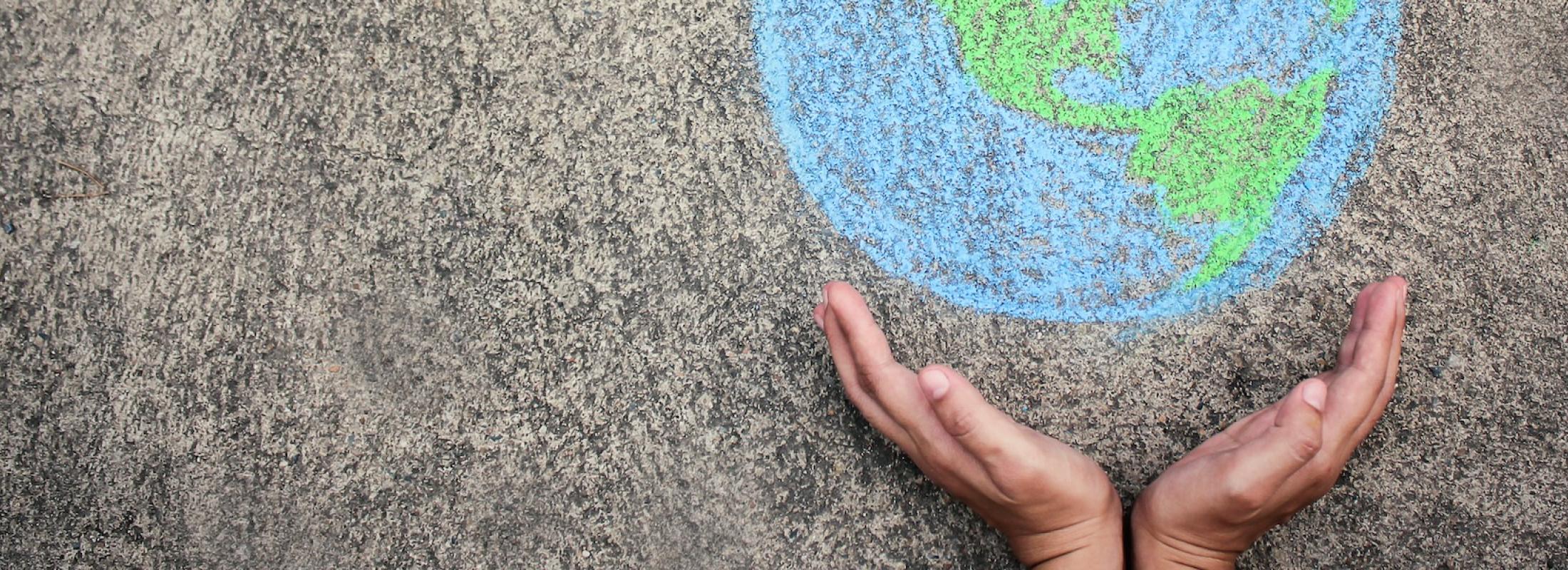 childs hands holding a chalk drawing of the world