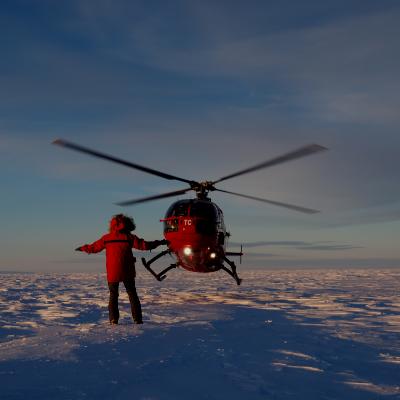 Helicopter landing with someone directing it over a snowy terrain