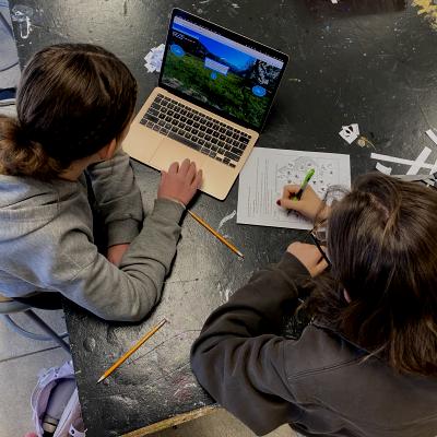 Two people writing and looking at a computer