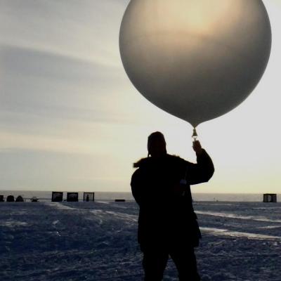 Person holding a clear balloon on an ice field with the sun in the back