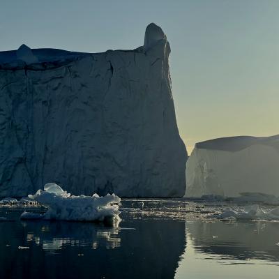 Ice berg floating on the ocean with the sun in the background