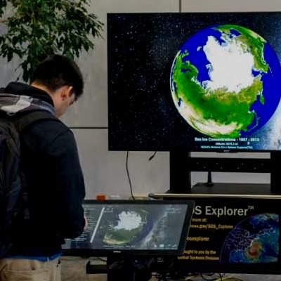 Person looking down at an interactive SOS exhibit board with the a globe on the tv in front of the person