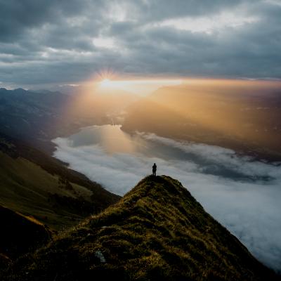 Person standing on top of mountain, sun rising in the back with ocean in the horizon