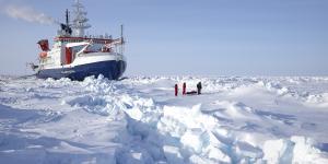 People playing in an Arctic ice field covering the ocean with boat behind them