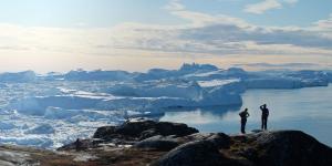 People standing on mountain side overlooking an ocean with ice bergs
