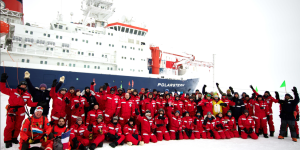 Mosaic team photo with boat behind them and wearing all red suits