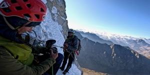 Two people on the side of a cliff climbing and one person filming the other