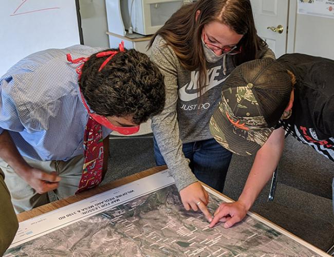 Three people looking at a map, two are point to a spot on the map