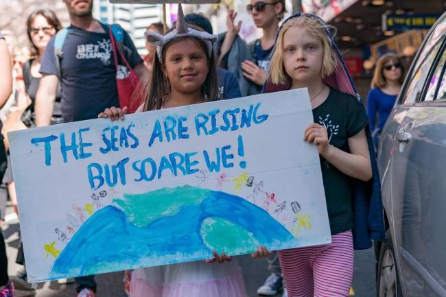 Two girls standing side by side holding a sign that reads "The seas are rising but so are we!"