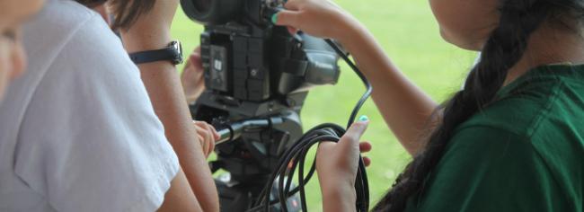 Close-up of people setting up a professional video camera, with one person adjusting controls and another holding cables