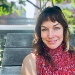 Headshot of Hilary Peddicord smiling, she is outside on a wooden bench with a tree behind her